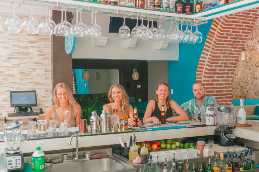 Group of friends sitting and smiling at a stylish bar counter with drinks and bottles.