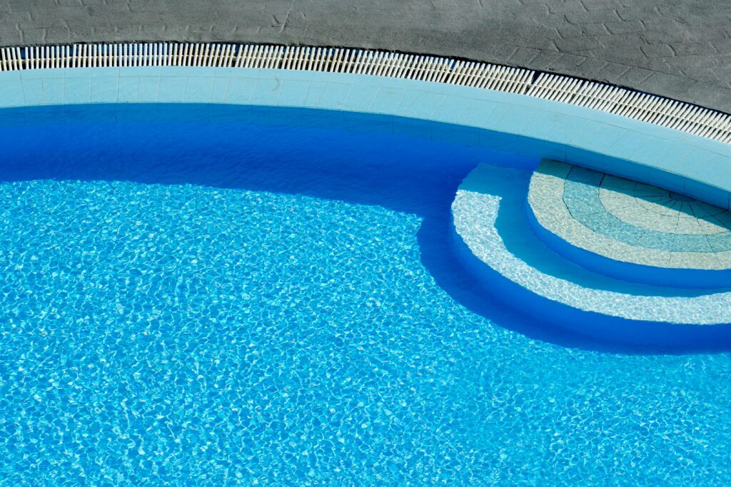 Sun-drenched swimming pool captured from above, showcasing clear blue water and elegant curves.